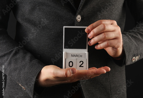 Business man in a jacket holding a calendar with the date March 1