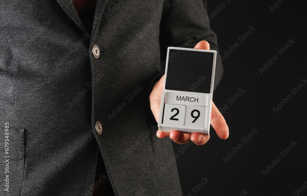 Business man in a jacket holding a calendar with the date March 29 Business man in a jacket holding a calendar with the date March 29