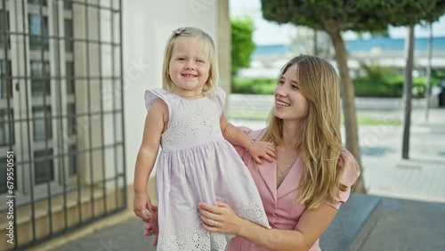 Joyful caucasian mum confidently standing on street, arms cradling her giggling daughter, both sharing a fun, positive outdoor moment in their favorite city.