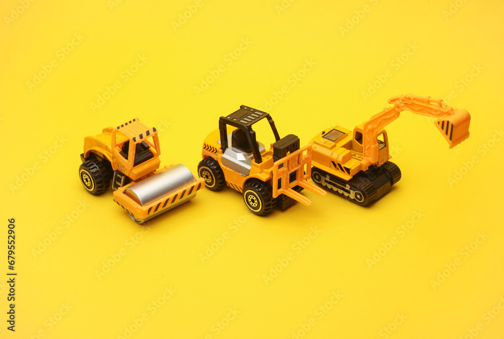 Toy forklift, asphalt paver and excavator on yellow background Toy forklift, asphalt paver and excavator on yellow background