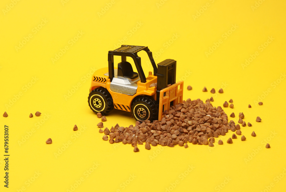 Fototapeta premium Miniature toy forklift and wheat grain on a yellow background.