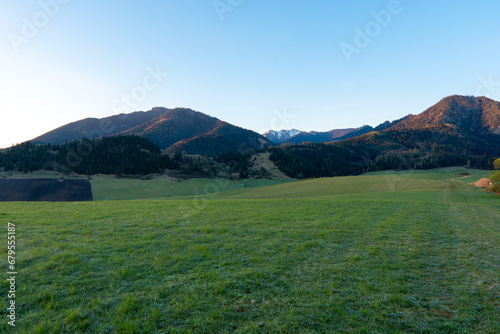 Obraz na płótnie green field in countryside at sunset in the evening light. beautiful spring landscape in the mountains. grassy field and hills. rural scenery w salonie