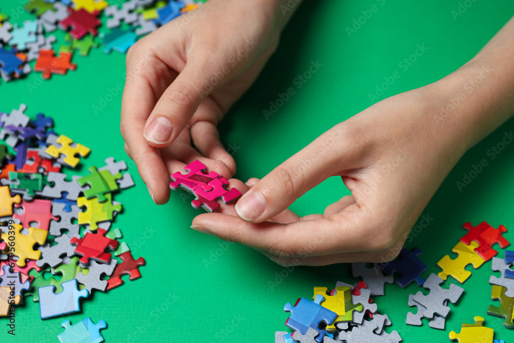 Сolored puzzles in hands on green background, close up Сolored puzzles in hands on green background, close up