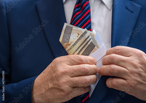 Człowiek w eleganckim garniturze chowa kopertę z pieniędzmi do kieszeni w marynarce 