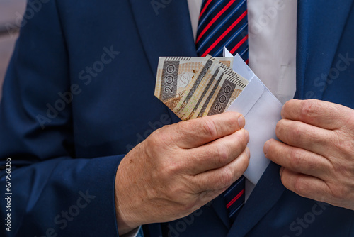 Elegancki mężczyzna chowa kopertę z polskimi banknotami do kieszeni