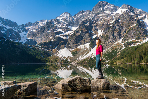 Young woman in red sportswear standing in the nature, mountain lake and range on the background, active life concept, summer time in Eye of the Sea lake in Tatra Mountains in Poland photo