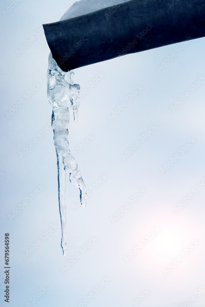 A large icicle hangs from a gutter in winter in sunny weather A large icicle hangs from a gutter in winter in sunny weather