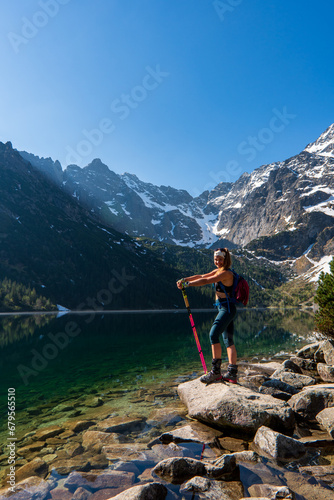 Young woman in red sportswear standing in the nature, mountain lake and range on the background, active life concept, summer time in Eye of the Sea lake in Tatra Mountains in Poland