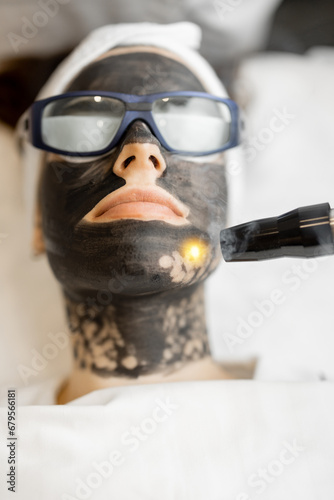 Fototapeta Naklejka Na Ścianę i Meble -  Beauty procedure of laser carbon peeling on woman's face. Close-up on client's face in carbon mask and protective eyeglasses. Concept of beauty facial treatments