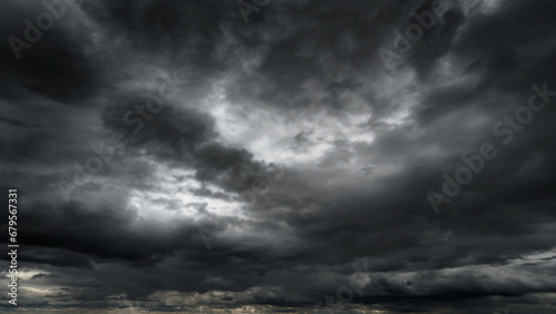 dark dramatic sky with black stormy clouds before rain or snow as abstract background  extreme weather  the sun shines through the clouds  high contrast photo