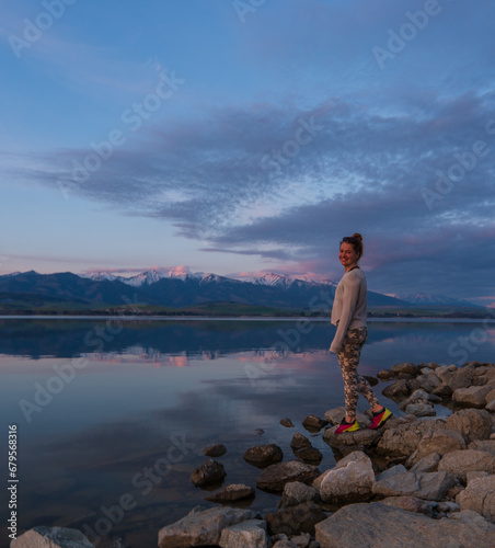 Woman traveler admiring the sunset on the shore of a lake in the mountains.