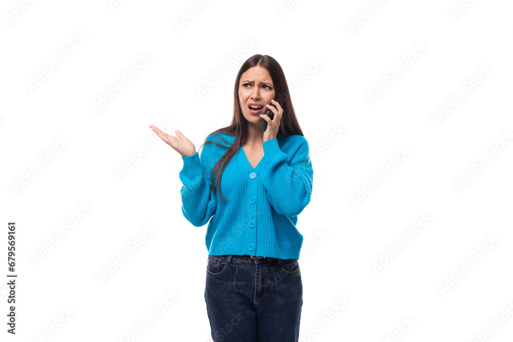 young beautiful European brunette woman dressed in a blue cardigan speaks on the phone while listening attentively to the interlocutor young beautiful European brunette woman dressed in a blue cardigan speaks on the phone while listening attentively to the interlocutor