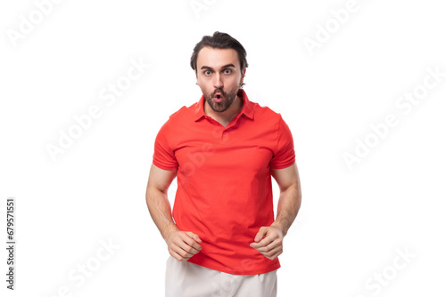 young surprised european brunette man with a beard dressed in a red t-shirt looks at the camera on a white background with copy space