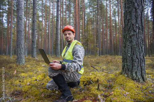 Forest engineer works in the forest with a computer. An ecologist carries out a tax assessment of a forest area.