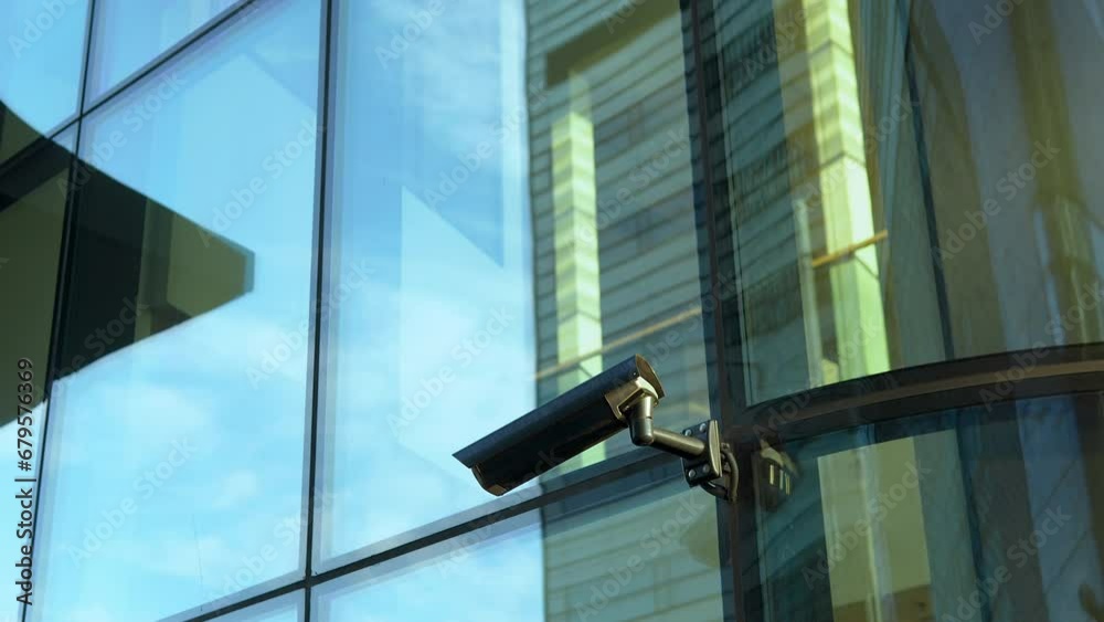 Surveillance camera attached to a modern building's reflective glass