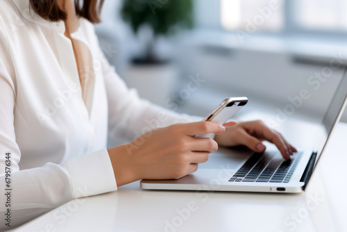 woman uses a cell phone while using laptop keyboard on white table