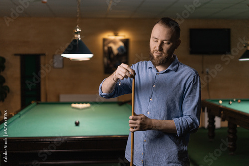 Male snooker player prepares to play billiards by rubbing his cue with chalk to prevent it from slipping. photo