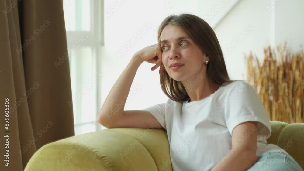 Positive, peaceful young woman is resting at home on the sofa, leaning back, breathing in fresh air, looking out the window into the distance, thinking, dreaming Positive, peaceful young woman is resting at home on the sofa, leaning back, breathing in fresh air, looking out the window into the distance, thinking, dreaming