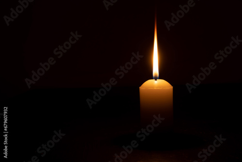A single burning candle flame or light glowing on a yellow candle isolated on red or dark background on table in church for Christmas, funeral or memorial service photo