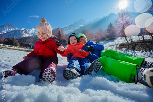 Siblings laughing, roll in snow at sunny snowy mountain camp