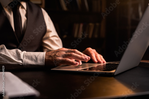 Concept of home office working. Close up businessman using laptop indoors. Business man wear formal waistcoat hands typing computer in dark room. Luxury expensive workplace