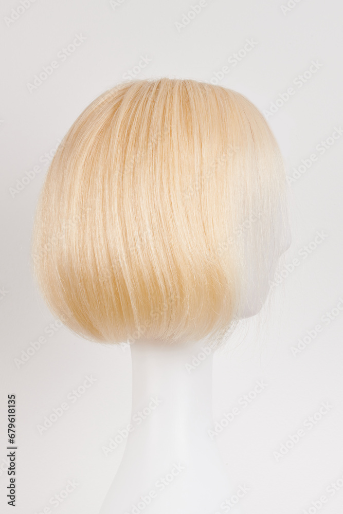 Natural looking blonde fair wig on white mannequin head. Short hair cut on the plastic wig holder isolated on white background, side view.