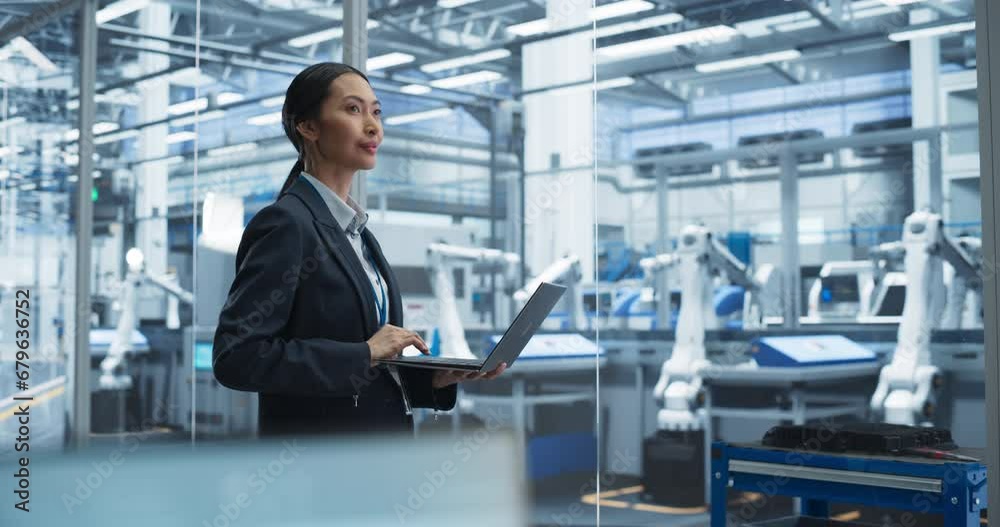 Beautiful Asian Female Engineer Standing Next to a Window in Office, Using Laptop Computer at an Electronics Factory. Machines are Undergoing Maintenance, Specialist Using an Online Software Beautiful Asian Female Engineer Standing Next to a Window in Office, Using Laptop Computer at an Electronics Factory. Machines are Undergoing Maintenance, Specialist Using an Online Software