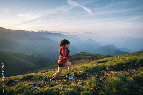 Female trail runner ascending alpine trail in the mountains at sunrise