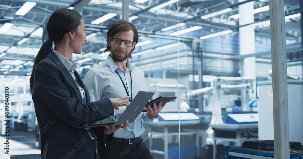 Portrait of a Cheerful Engineer and Happy Asian Scientist Using Laptop and Tablet Computers, Talking in a Factory Facility with Robots Producing Modern Electronic Components for Different Industries Portrait of a Cheerful Engineer and Happy Asian Scientist Using Laptop and Tablet Computers, Talking in a Factory Facility with Robots Producing Modern Electronic Components for Different Industries