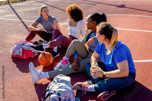 Diverse group of young woman sitting on court resting afrer playing basketball outdoors. photo