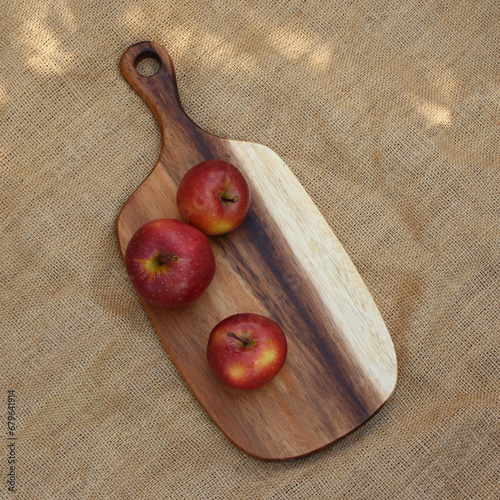 Three red apples on a wooden cutting board