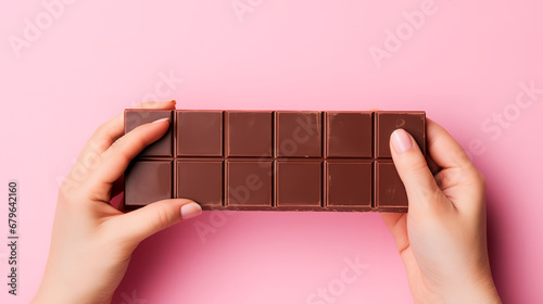 Photograph from above of a person's hand holding a chocolate, plain background