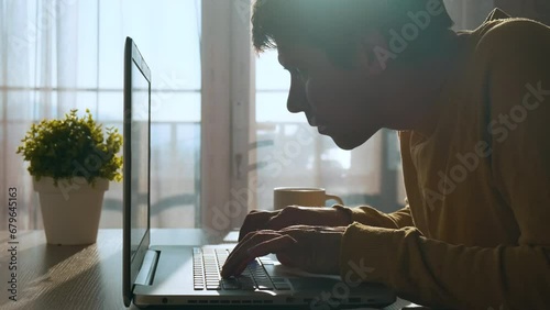 Focused concentrated young man typing on keyboard while working on laptop computer at home. Serious male professional trader and broker working online on computer with stock market photo
