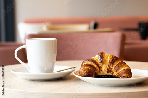 Croissant and a cut of coffee on a cafeteria table