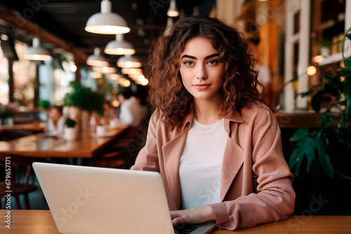 Young woman working on laptop in cafeteria. Designer freelancer or student work on laptop at table.