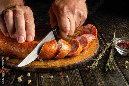 A man hands use a knife to cut meat sausage for making sandwiches. Delicious fast food idea for a snack.