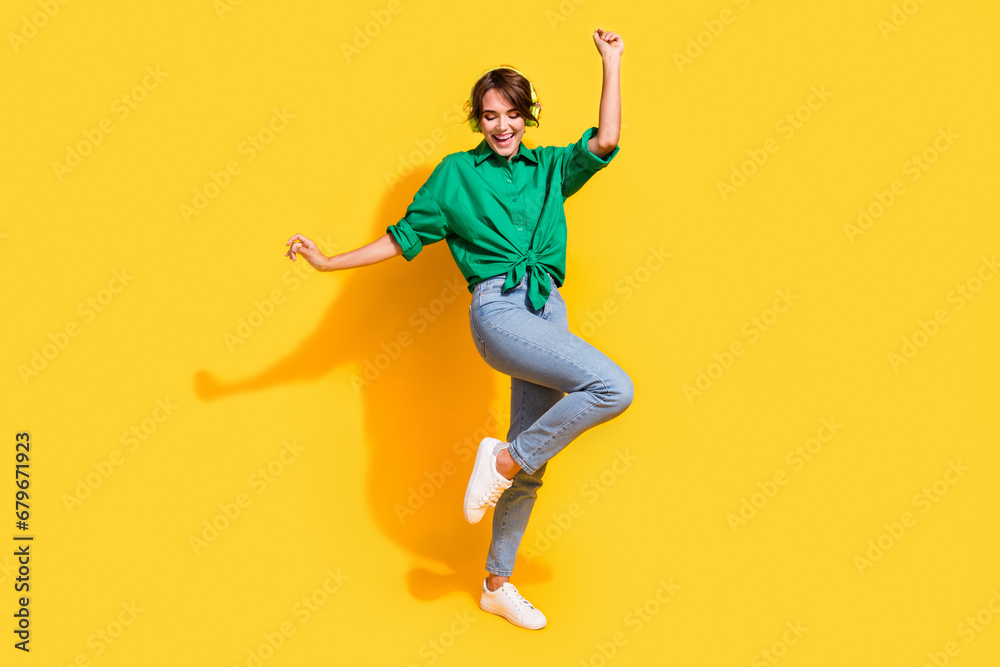Full length photo of pretty cheerful girl dressed green shirt headphones dancing having fun isolated yellow color background