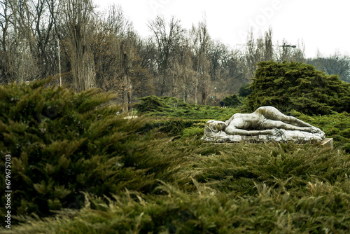 A serene sculpture of a sleeping woman graces the autumn landscape, surrounded by trees adorned with warm-hued foliage. Nature and art harmonize in a tranquil seasonal tableau