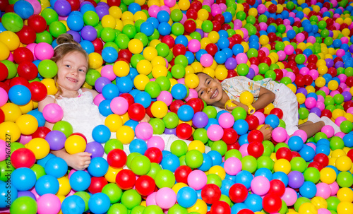 Happy girl playing in ball pit on birthday party in kids amusement park and indoor play center. Child playing with colorful balls in playground ball pool.