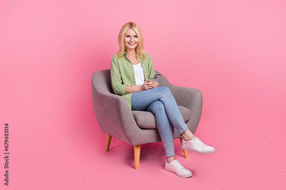 Full size photo of attractive positive lady sitting comfort chair use smart phone isolated on pink color background
