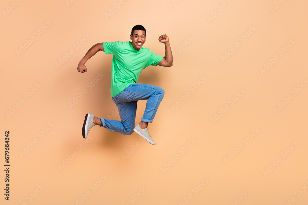 Full size photo of optimistic active guy dressed green t-shirt denim pants fast running in empty space isolated on beige color background