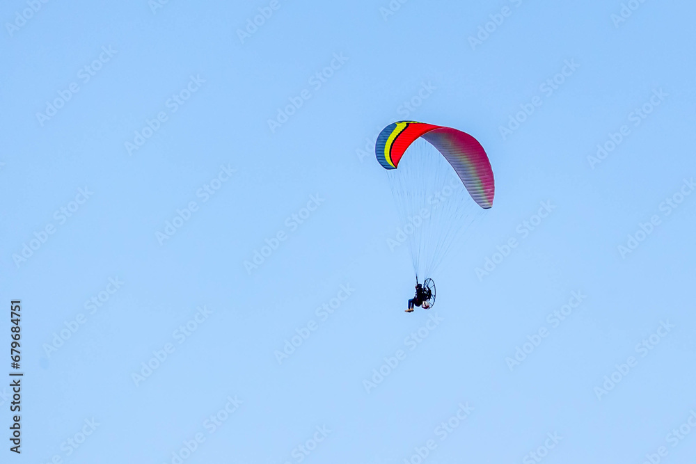 A Powered paragliding also knows as Paramotor flying through the blue sky. Sport. Leisure. Adventure. A Powered paragliding also knows as Paramotor flying through the blue sky. Sport. Leisure. Adventure.