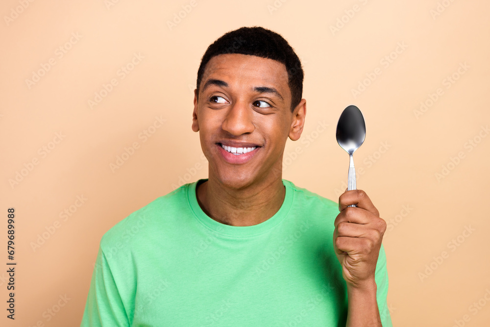 Photo portrait of attractive young man hold spoon look empty space wear trendy green clothes isolated on beige color background Photo portrait of attractive young man hold spoon look empty space wear trendy green clothes isolated on beige color background