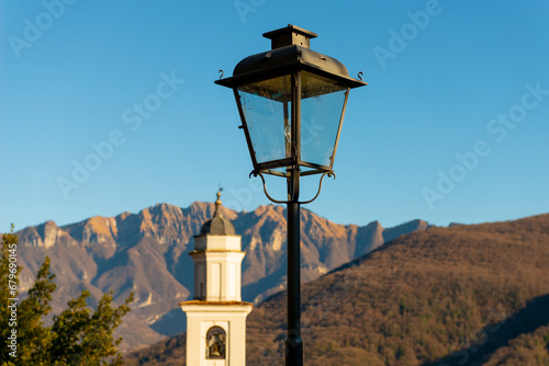 Church Tower of Saints Fedele and Simone and Street Lamp with Mountain in a Sunny Day in Vico Morcote, Ticino in Switzerland. photo