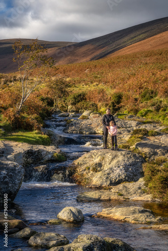 Mother and daughter standing on a stone next to Dargle River, flowing to Powerscourt Waterfall. Family hiking in Wicklow Mountains, autumn, Ireland