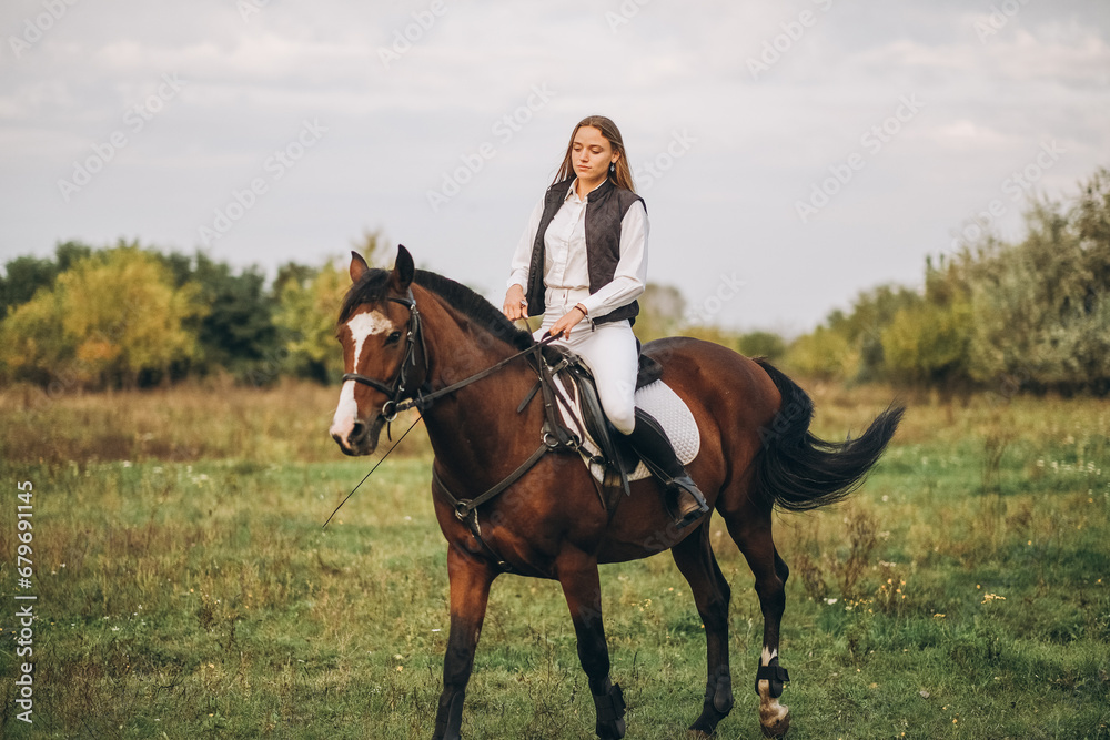 Young beautiful blonde woman jockey rides a brown horse in a meadow at sunset in summer. Preparing for an equestrian competition. Young beautiful blonde woman jockey rides a brown horse in a meadow at sunset in summer. Preparing for an equestrian competition.