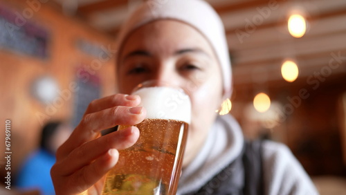 Woman drinking draft beer at restaurant during cold season. Close-up face of person drinks refreshing alcoholic beverage photo