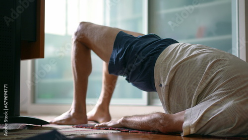 Senior man taking care of his lower back in morning exercise routine to relieve back pain. Elderly caucasian 70s person doing bridge position, spine health in old age © Marco