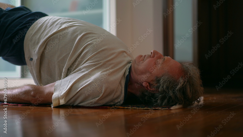 Senior man taking care of his lower back in morning exercise routine to relieve back pain. Elderly caucasian 70s person doing bridge position, spine health in old age Senior man taking care of his lower back in morning exercise routine to relieve back pain. Elderly caucasian 70s person doing bridge position, spine health in old age