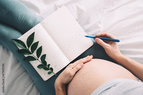 Pregnant woman with beautiful belly makes notes or check list in paper diary. Concepts of preparation for baby birth, tips for a healthy pregnancy. photo